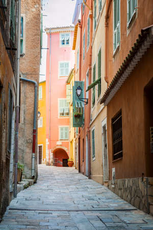 Narrow cobblestone street with bright buildings in medieval town Villefranche-sur-Mer on French Riviera, France.の写真素材