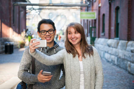 Two young people taking a selfie with smartphone on city street