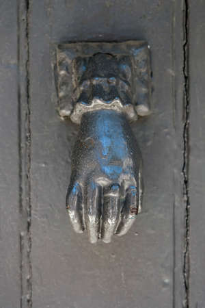 Antique metal door knocker shaped like a hand on old door in Toulouse, France, closeup.