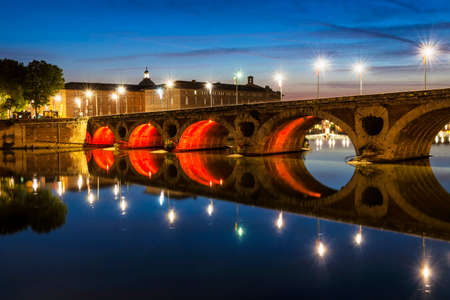 Evening view of historic Pont Neuf in Toulouse, France, with illuminated arches over Garonne River.の写真素材