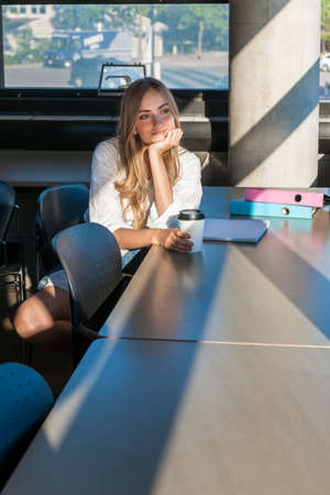 Young woman student with books and binders studying in a study area of university or college campus...