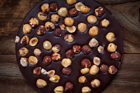 Round artisanal dark chocolate bar with whole hazelnuts on rustic wood background, overhead viewの写真素材