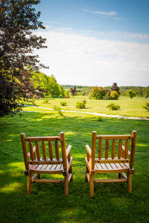 Two wooden chairs on lush green lawn with view of countryside in summerの写真素材