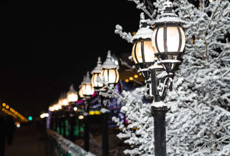 Vintage street lights lit on the streets of the city at night. Winter city landscape. Snow-covered fence and lamps.の写真素材