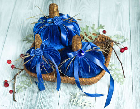 Beautiful blue pumpkins made of velvet fabric are decorated with various elements and ribbons in a small wicker basket. Home decor for the Halloween holidayの写真素材