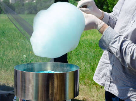Preparation of cotton candy. A man in cooking gloves prepares sweets in the Park.の写真素材