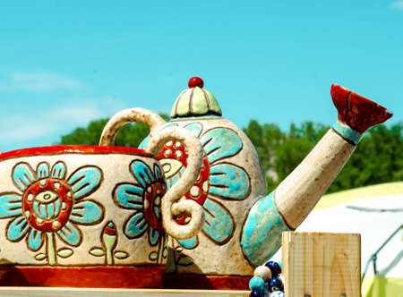 painted ceramic dishes stand against blue sky. Teapot and bright mug.の写真素材