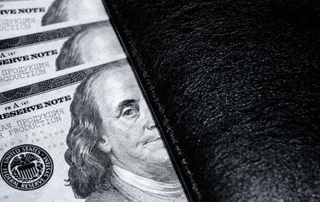 Black-and-white close-up photo of dollars. American paper banknotes. There are several hundred-dollar bills under black wallet. Cash. Finance.の写真素材