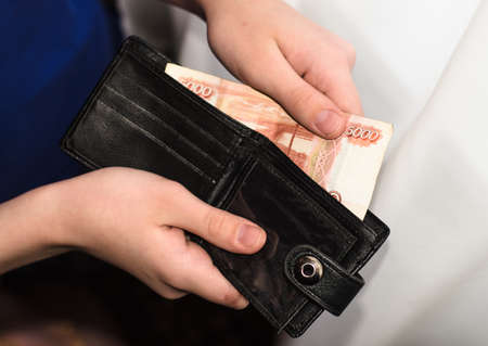young man takes out 5000-ruble banknote from black wallet. Russian cash. Finance.の写真素材
