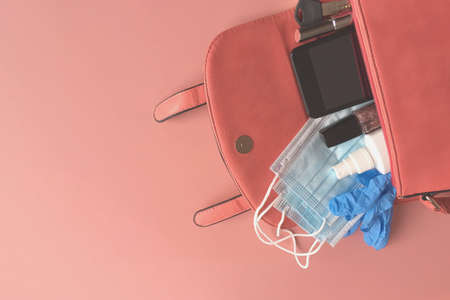 Open womens purse contains rubber gloves, medical masks, antivirus spray, smartphone, lipstick, keys, nail polish on pink background. New normality.Copyspaceの写真素材