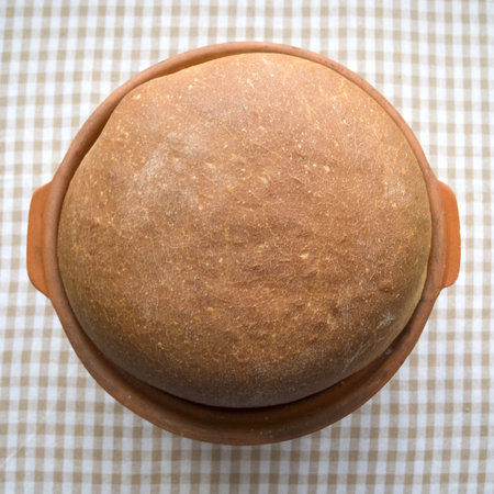 Fresh homemade wheat bread in clay form on a linen tablecloth. From above. Crop plan.