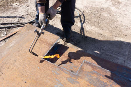 Metal sheet cutting, worker with gas cutter cuts metal square billet from a sheet of metal, outdoor