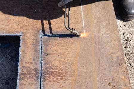 Metal sheet cutting, worker with gas cutter cuts metal square billet from a sheet of metal, outdoor