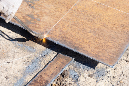Metal sheet cutting, worker with gas cutter cuts metal square billet from a sheet of metal, outdoor