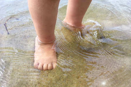 Toddler's legs on the ankle in the water go on the sand on the beach