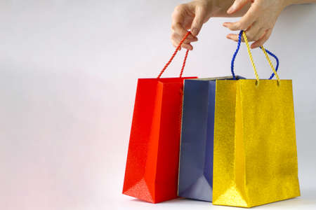 Womens hands hold red, blue and gold paper bags with purchases on a white background. Copyspaceの写真素材