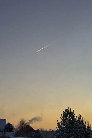 Plane trail in the frosty morning sky, smoke from a chimney, trees in the snow