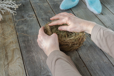 Handmade master class Easter nest made of natural dry grass and used cardboard. The hands of an elderly woman show step by step how to make an Easter nest on wood backgroundの写真素材