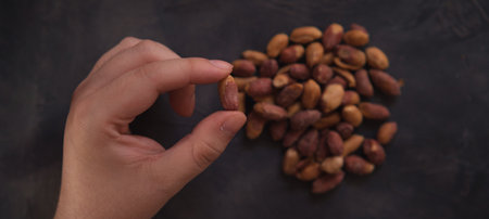 Female hand showing a roasted peanut over dark background. Healthy food.