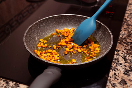 Fresh chopped carrots cooking on frying pan on induction stove. Cooking delicious dish with vegetables at home.の写真素材