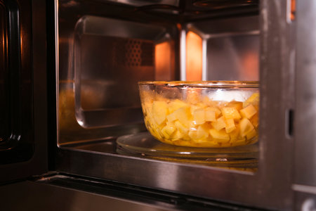 Putting a bowl with raw peeled potatoes in microwave. Cooking at home. Fresh homemade food.の写真素材