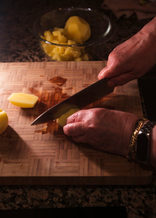 Woman chopping fresh peeled potatoes over wooden cutting board. Delicious homemade food. Spanish cuisine.の写真素材