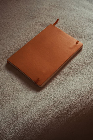 Orange leather notebook mockup on white textured surface.の写真素材