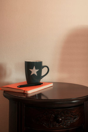 Gray mug with orange notebook and a pen resting on wooden table.