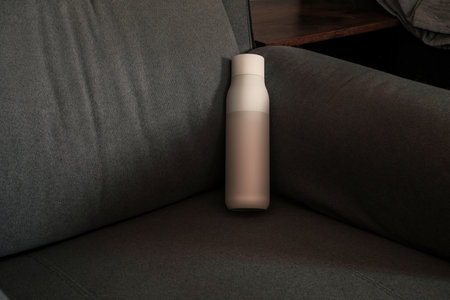 White water bottle resting on light gray sofa. Clean bottle for mockup use.