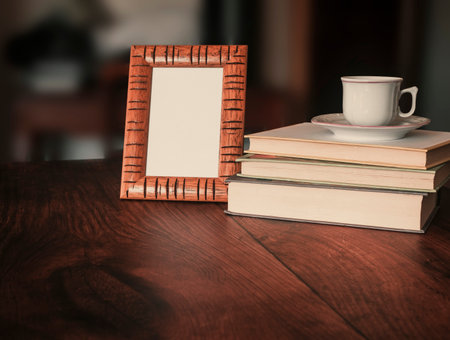 Vertical wooden picture frame mockup on desk with stack of books and coffee cup.