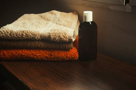Amber glass bottle mockup for cosmetics next to stacked towels on wooden surface.