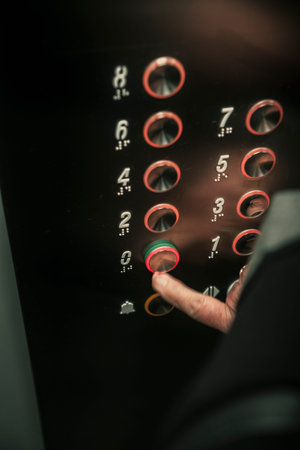 Close up of senior woman hand pressing an elevator button with braille numbers.