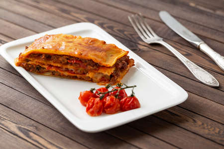 Tasty lasagna with meat covered with cheese, served with baked tomatoes on a white plate.の写真素材