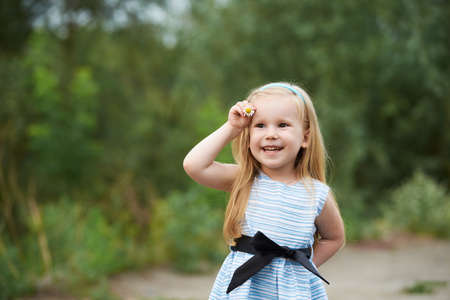 Young girl with flower. Blue dress. Smiling blondの写真素材