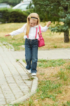 Young girl walk on curb. Jeans, ping bag.の写真素材