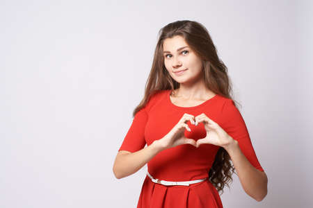 Portrait beautiful girl. Gesture heart. Brunette. Red dress. White background.の写真素材