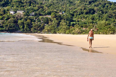 Old man. Walking along beach. Warm sand.の写真素材