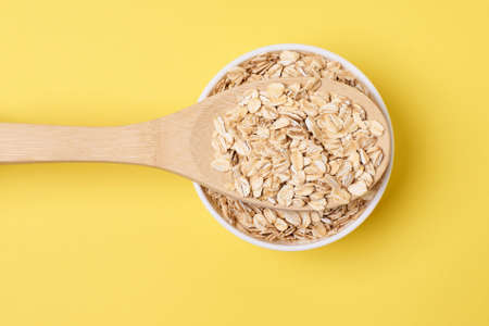 Healthy eating. Wooden spoon. Oat flakes. Yellow background.の写真素材