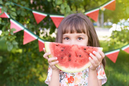 Little girl. Juicy red watermelon slice. Summer sunny day. Bright Grass.の写真素材