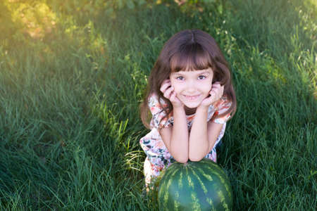 Large striped watermelon. Little sweet girl. Juicy green grass. Summer landscape.の写真素材