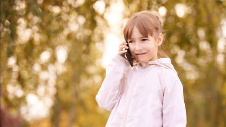 Little girl talk phone. Autumn background.の写真素材