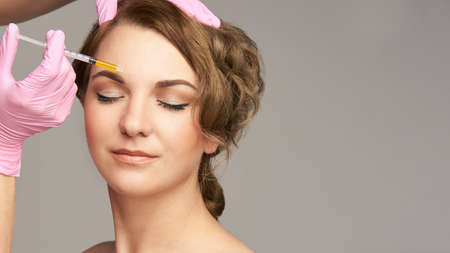 Face needle injection. Young woman cosmetology procedure. Doctor gloves. Brow.の写真素材