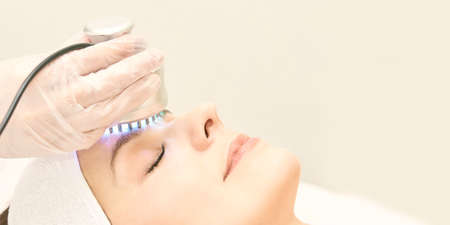 Light infrared therapy. Cosmetology head procedure. Beauty woman face. Cosmetic salon device. Facial skin rejuvenation.の写真素材