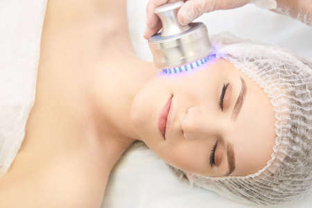 Light infrared therapy. Cosmetology head procedure. Beauty woman face. Cosmetic salon device. Facial skin rejuvenation.の写真素材