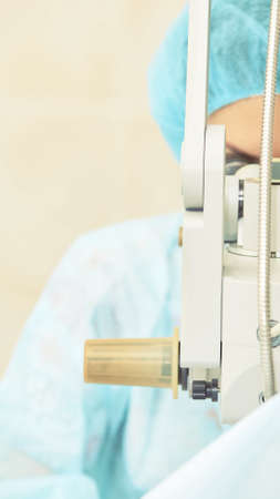 Pretty doctor woman portrait. Ophthalmology laser microscope operation. Clinic room. Patient eye...