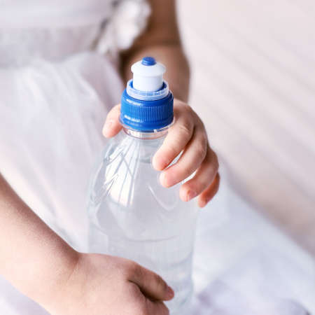 Young little girl hold water bottle. Kid drink cold fresh. Thirsty female person.の写真素材