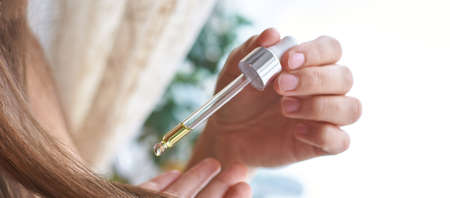Long hair care routine. Oil for hair. Girl holding dropper with castor mask near end. Bathroom natural protectionの写真素材