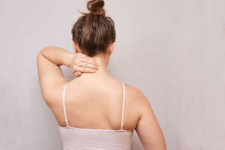 Girl hold hand near neck. Back view. Female head and shoulder. Home self massage. Young woman arm. Medical osteoporosis conceptの写真素材