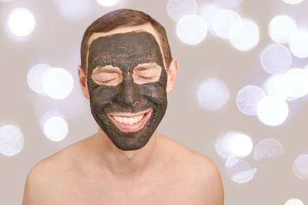 Black Clay Mask on Guy Face. Cosmetology man portrait with mud healthy scrub. Coal nature eco masque. Dermatology mud. Home skin care routine. Skincare male treatment. Pure ecology crack product.の写真素材
