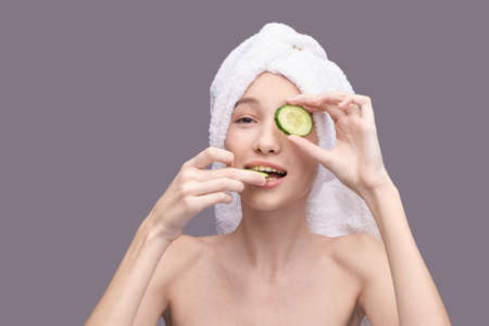 Young girl holding cucumber slice in hand. Nature mask concept. Face skincare routine. Lifting effect. Happy woman portrait. Dermatology homemade healthcare procedure.の写真素材